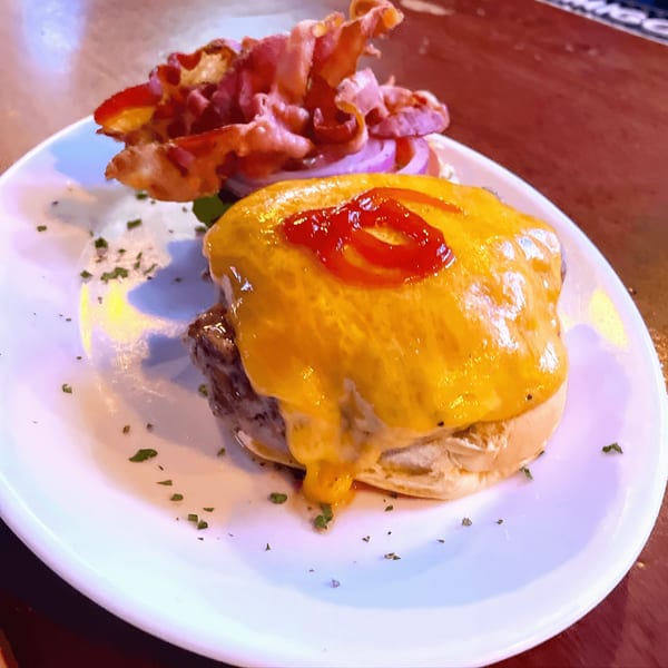 Cheeseburger with melted cheddar, ketchup, bacon, and red onion on a white plate at Overlook.