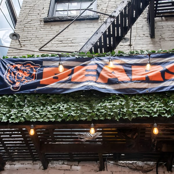 A Chicago Bears banner hangs above a green ivy wall, with string lights and a fire escape.
