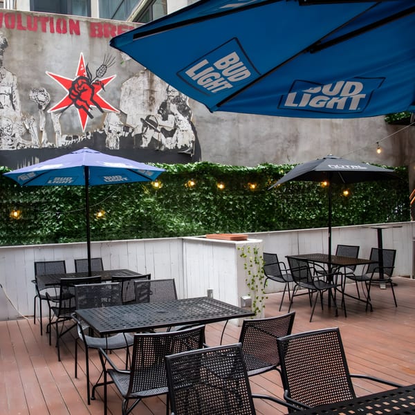 Overlook's outdoor patio features black metal tables and chairs under Bud Light and NUTRL umbrellas, with a mural backdrop.
