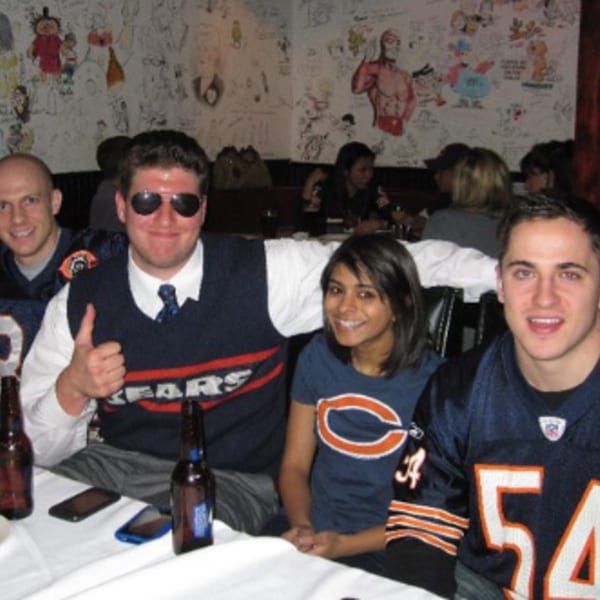 Four friends in Chicago Bears gear, with beers, at a table in a sports bar.