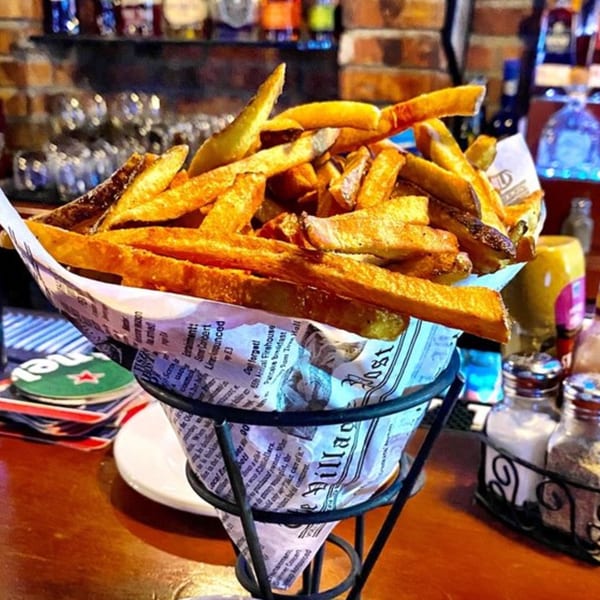 A metal cone filled with crispy french fries, lined with newspaper, on a bar counter at Overlook.