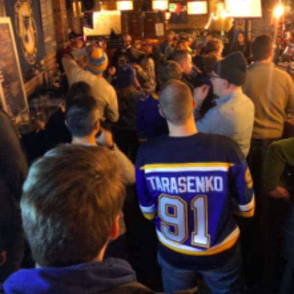 A crowded sports bar with patrons watching a game, one wearing a "Tarasenko 91" jersey.