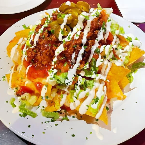 A large plate of Overlook's nachos, topped with meat, cheese, jalapeños, lettuce, and sour cream.
