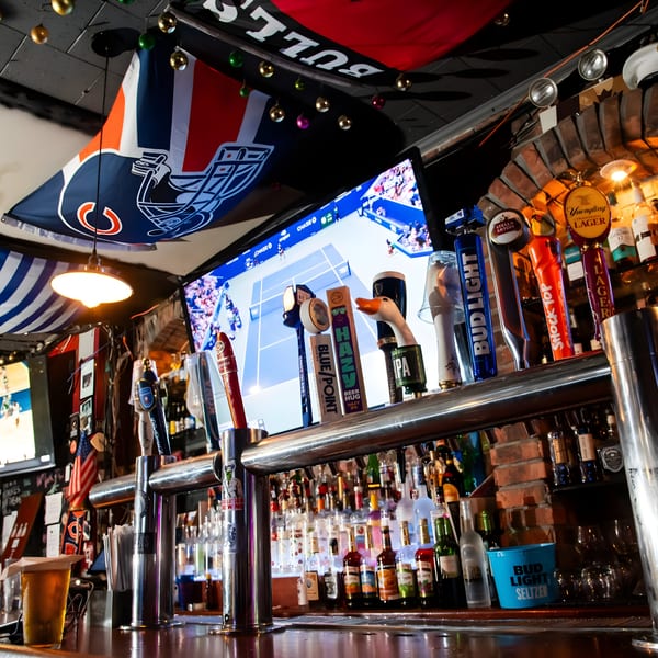 A sports bar interior with beer taps, liquor bottles, and a TV showing a tennis match.