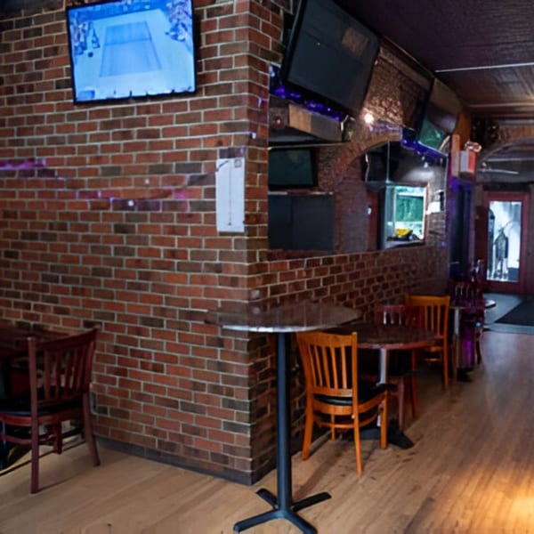Interior of Overlook sports bar with brick walls, wooden chairs, high-top tables, and a TV showing tennis.