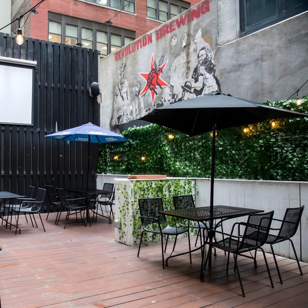 Overlook's outdoor patio with black tables and chairs, a Bud Light umbrella, and Revolution Brewing mural.