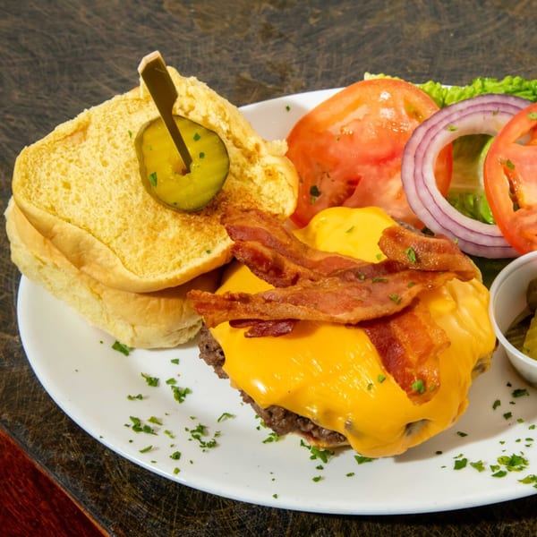 A bacon cheeseburger with a side of lettuce, tomato, and red onion on a white plate.
