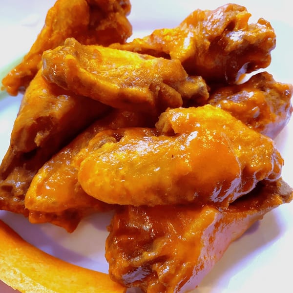 A close-up of several glossy, orange-sauced chicken wings on a white plate with a carrot stick.